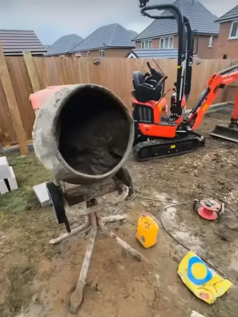 A back garden dug out to bare ground, with the mixer and a mini digger