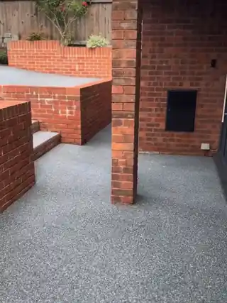 A finished grey resin drive running past red brick steps and a brick pillar