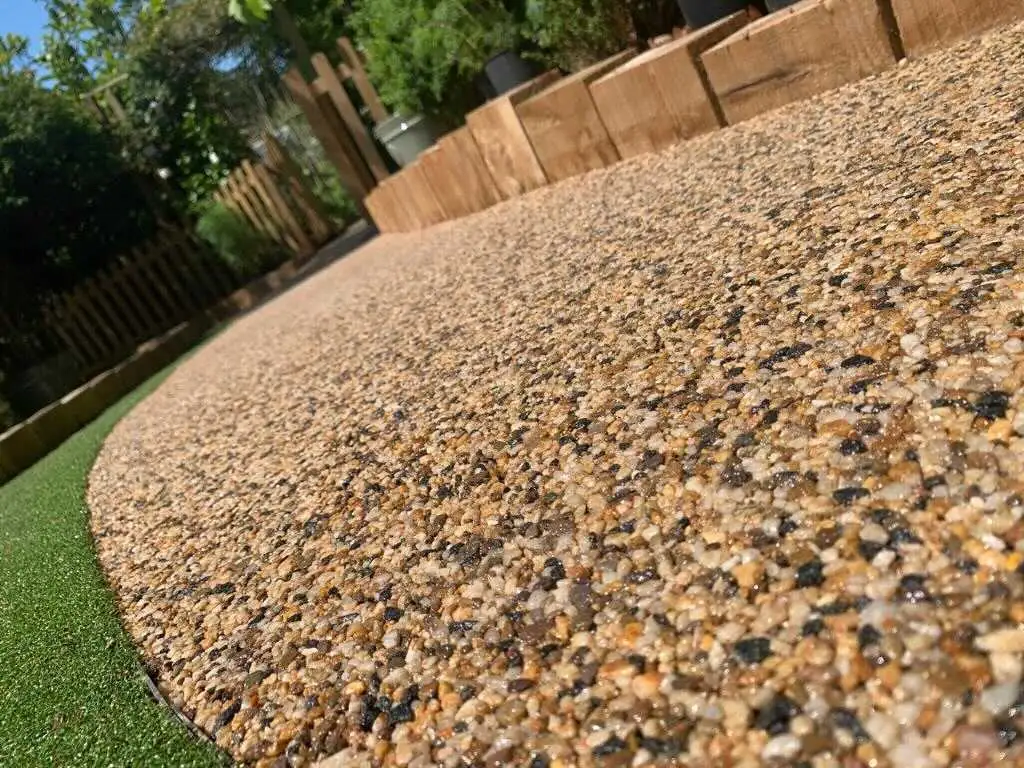 A golden resin bound driveway sweeping in a long curve beside artificial lawn and a sleeper retaining wall