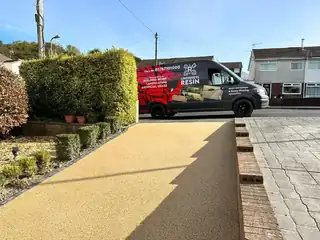 A golden resin driveway running past a trimmed hedge to the road, with the works van parked on it