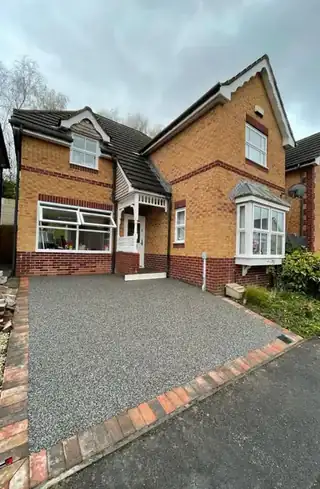A grey resin driveway laid in front of a red brick detached house, edged with brick