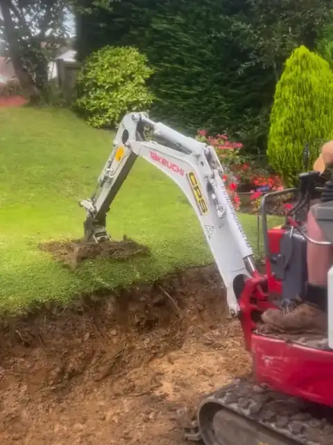 A mini digger taking out the old ground beside the lawn