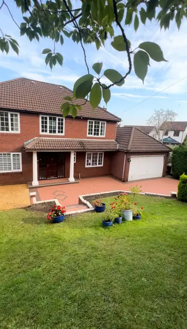 A terracotta resin driveway curving up to a red brick detached house, with a clipped lawn alongside