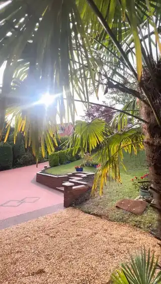 A terracotta resin path running past brick planting beds and palms to a set of steps