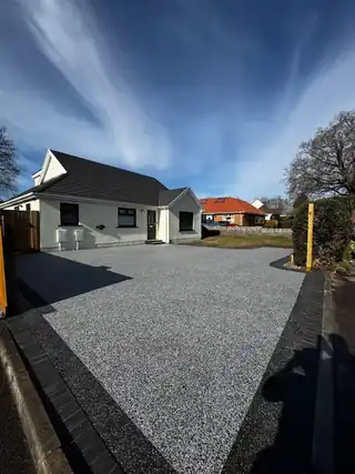 A wide grey resin driveway running the full frontage of a white rendered bungalow