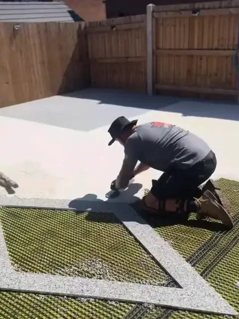 An installer kneeling to trowel a cream resin patio with a grey diamond inlay