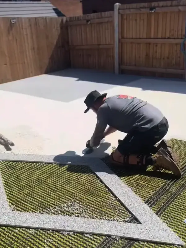 An installer kneeling to trowel a cream resin patio with a grey diamond inlay