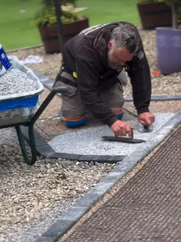 An installer trowelling a silver resin path beside the lawn