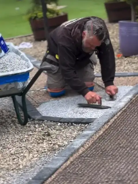 An installer trowelling a silver resin path beside the lawn