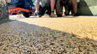 Installers kneeling at the edge of a freshly trowelled golden resin surface, photographed low from the aggregate