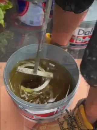 Resin being mixed in its tub on site, the paddle turning a slow amber swirl
